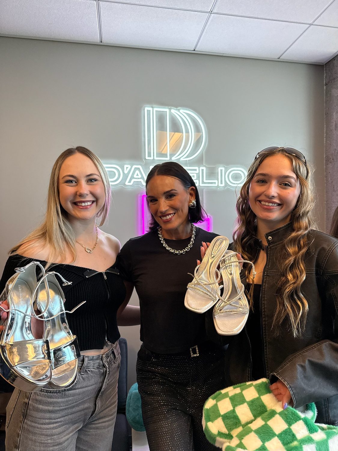 Creators posing with D'Amelio Footwear shopping bags in front of the brand's neon sign at the launch event