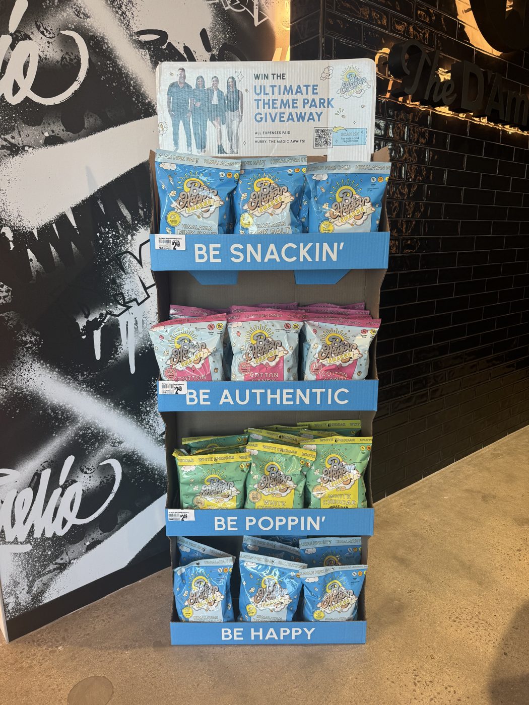 A Be Happy Snacks retail display, stocked with Himalayan Pink Salt, Cotton Candy, and White Cheddar popcorn